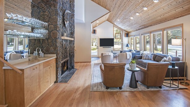 Ein modernes Wohnzimmer mit Kamin aus Stein, Holzbalkendecke und großen Fenstern.