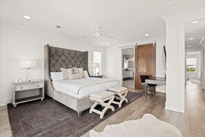 A modern bedroom with a large bed, a nightstand, a desk, and a bathroom visible through an open door.
