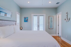 A bedroom with a large bed, a nightstand with a lamp, a painting on the wall, a door with a mirror, and a ceiling light.