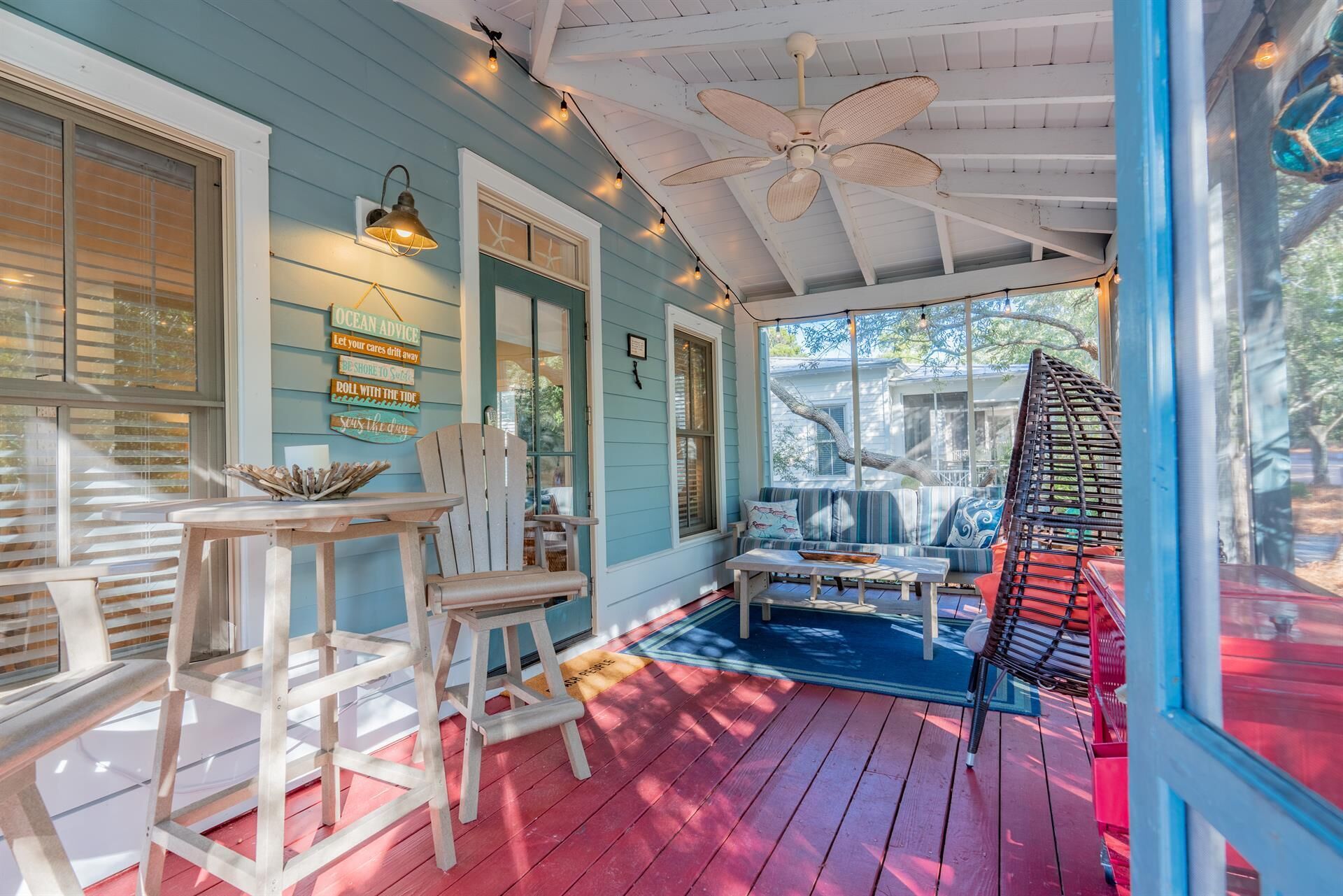 A covered porch with a ceiling fan, wooden chairs, a table, and a blue sofa.