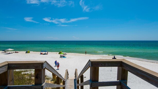 A wooden deck leading to a beach with white sand and clear turquoise water.