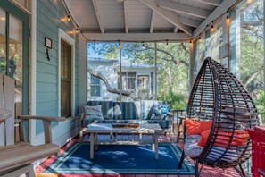 A covered porch with a swing chair, a cushioned bench, and a table.