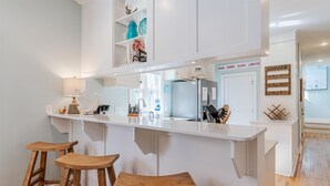 A kitchen with a central island, bar stools, a refrigerator, and a coffee sign.