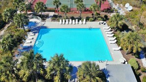 Vue aérienne d’un complexe hôtelier doté d’une piscine entourée de palmiers et d’un court de tennis.