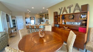 Un coin repas avec une table et des chaises en bois, une cuisine à l’arrière-plan, et un mur orné d’une enseigne « YATA » et d’une autre indiquant « GRAMMONT ST ».