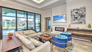 Ein geräumiges Wohnzimmer mit einer großen Couch, einem Couchtisch und einem Kamin. Große Fenster bieten einen Blick ins Freie.