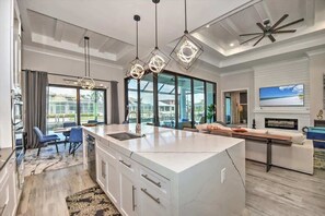 A modern kitchen with a large island, pendant lighting, and a view of the outdoors. - Luxury canal home w/ heated pool & spa! (Marco Island)