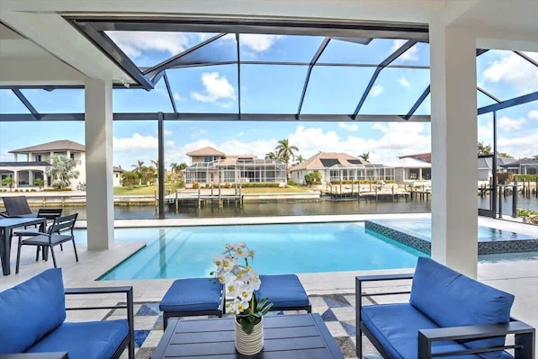 A poolside area with lounge chairs and a table, overlooking a swimming pool and a view of other buildings. - Luxury canal home w/ heated pool & spa! (Marco Island)