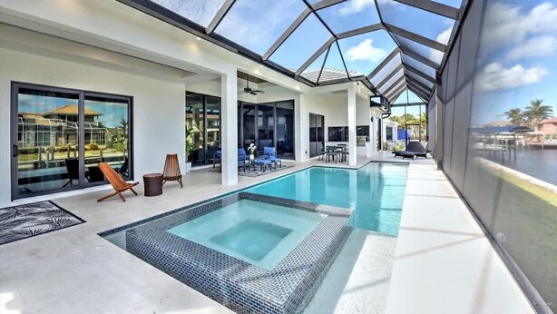 Ein moderner Poolbereich im Innenbereich mit Glaswänden, der einen ungehinderten Blick ins Freie bietet, und einer Lounge mit Liegestühlen und Tischen.