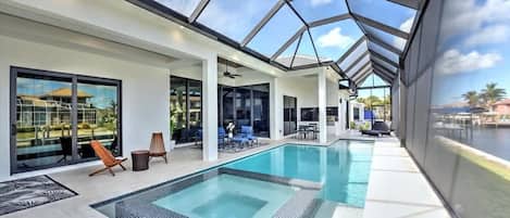 Un área de piscina interior moderna con paredes de vidrio, vistas despejadas al exterior y una zona de estar con sillones y mesas.
