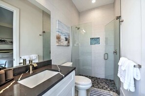 A modern bathroom with a glass-enclosed shower, a large mirror, and a white toilet.