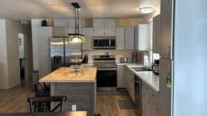 Een moderne keuken met roestvrijstalen apparatuur, een houten eettafel en lichtkleurige keukenkastjes.