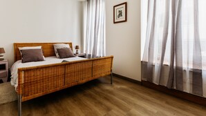 Ein Schlafzimmer mit einem Korbmöbelbett, einem Nachttisch mit Lampe und transparenten Vorhängen.
