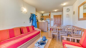 A compact living space with a red sofa, wooden dining table, and a kitchenette in the background. - Les Balcons du Soleil 4013 (Les Deux Alpes)