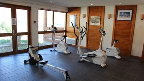 A fitness center with exercise equipment, large windows, and wooden paneling. - Les Balcons du Soleil 4013 (Les Deux Alpes)