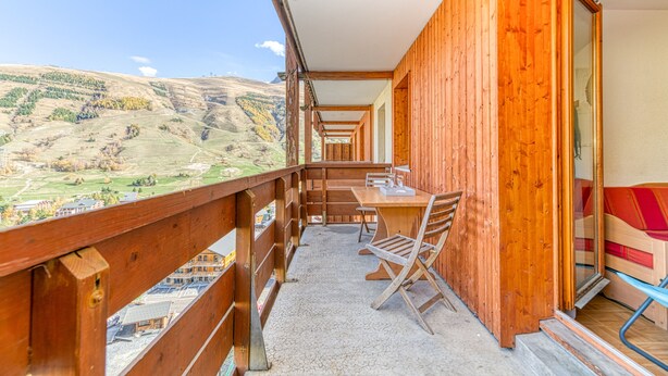 A wooden balcony with a table and chairs, offering a view of a mountainous landscape. - Les Balcons du Soleil 4013 (Les Deux Alpes)
