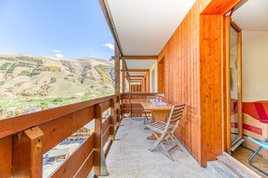 Un balcon en bois, agrémenté d’une table et de chaises, d’où l’on peut admirer un paysage montagneux.