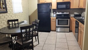 A compact kitchen with a dining table and chairs, a refrigerator, an oven, and wooden cabinets.