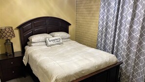 A neatly made bed with a pillow that reads "happiness is homemade" and a lamp on a bedside table.