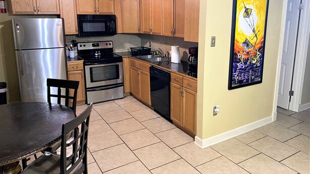 A kitchen with wooden cabinets, stainless steel appliances, a tiled floor, and a dining table with chairs.
