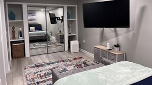 Un dormitorio moderno con cama, televisión montada en la pared, armario y mesita de noche con lámpara.