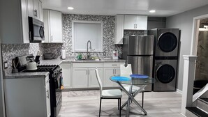Una cocina moderna con armarios blancos, un refrigerador de acero inoxidable, un horno doble y un lavamanos con grifo. Hay una mesa de vidrio con dos sillas y un mantel individual azul.