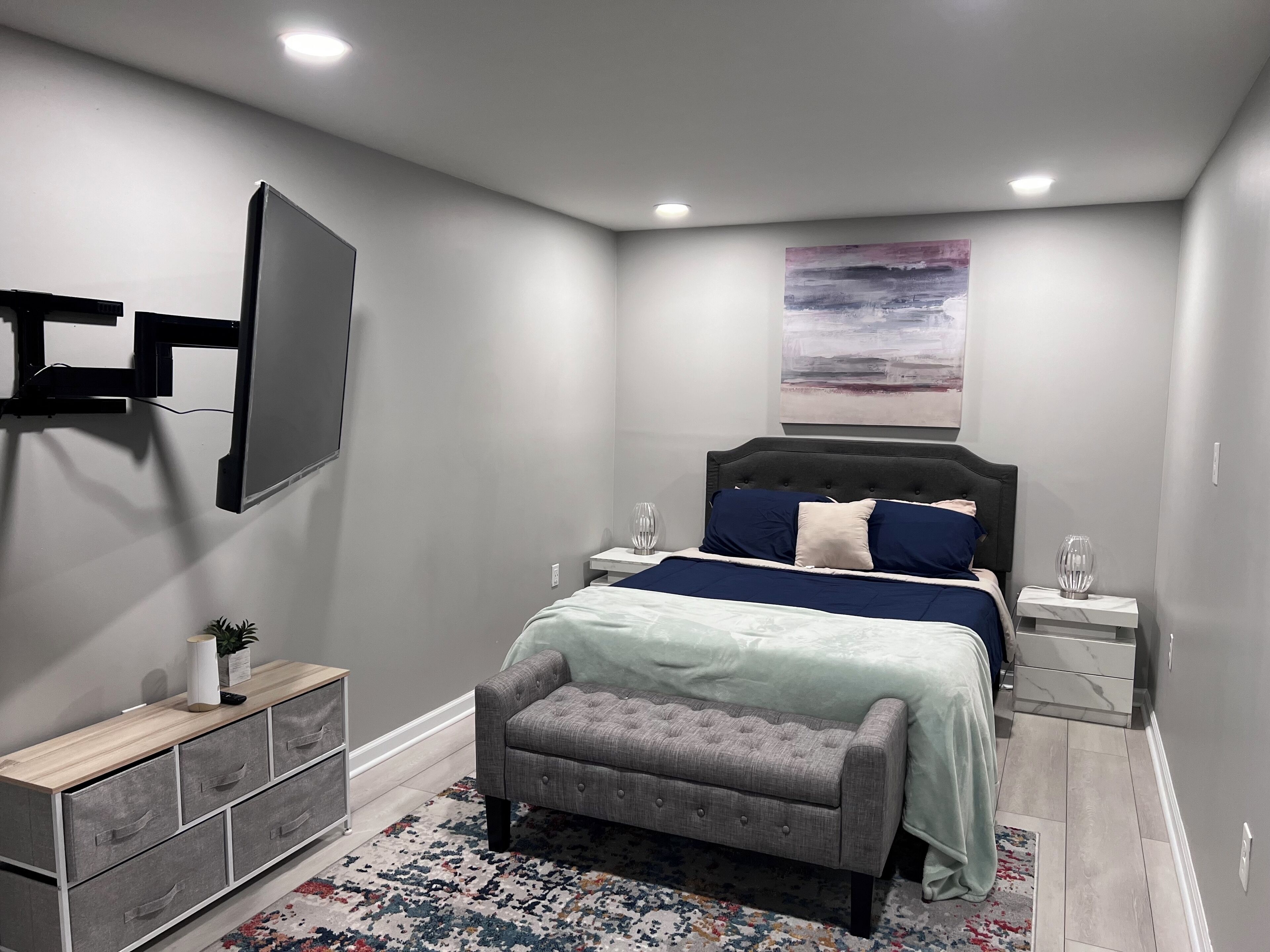 Een moderne slaapkamer met een groot bed, nachtkastjes, een bankje, een televisie en een schilderij aan de muur.