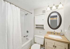 A bathroom with a bathtub, toilet, sink, and a mirror with lights above. - Wight Bay 440 by Seaside Vacations & Sales (Ocean City)