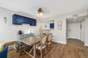 A dining area with a wooden table and chairs, a blue cabinet, and a ceiling fan. - Wight Bay 440 by Seaside Vacations & Sales (Ocean City)