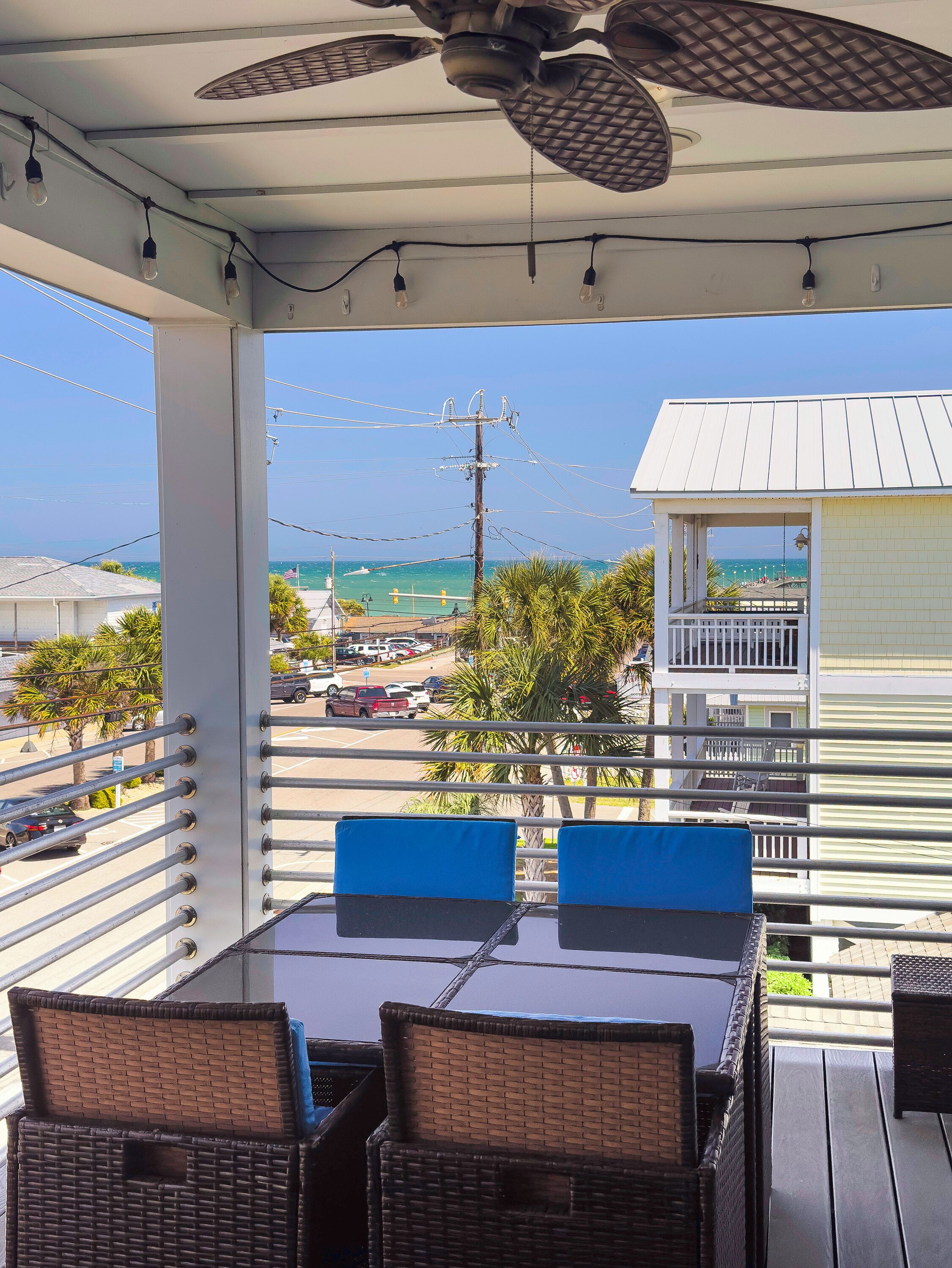 A covered outdoor seating area with a table and chairs, overlooking a beach and a parking lot.