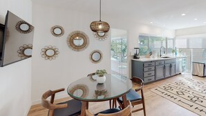 A modern kitchen with a large window, a dining area with a glass table, and decorative wall mirrors.