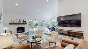 A spacious living room with a fireplace, comfortable seating, a large TV, and a view of the outdoors.
