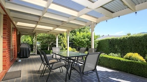 Une terrasse extérieure avec une table et des chaises à plateau en verre, un barbecue et un mur en briques.