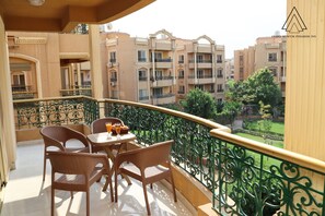 A balcony with wicker furniture and a table, overlooking a garden and residential buildings. - Grand Museum Pyramids Inn (Kirdasah)