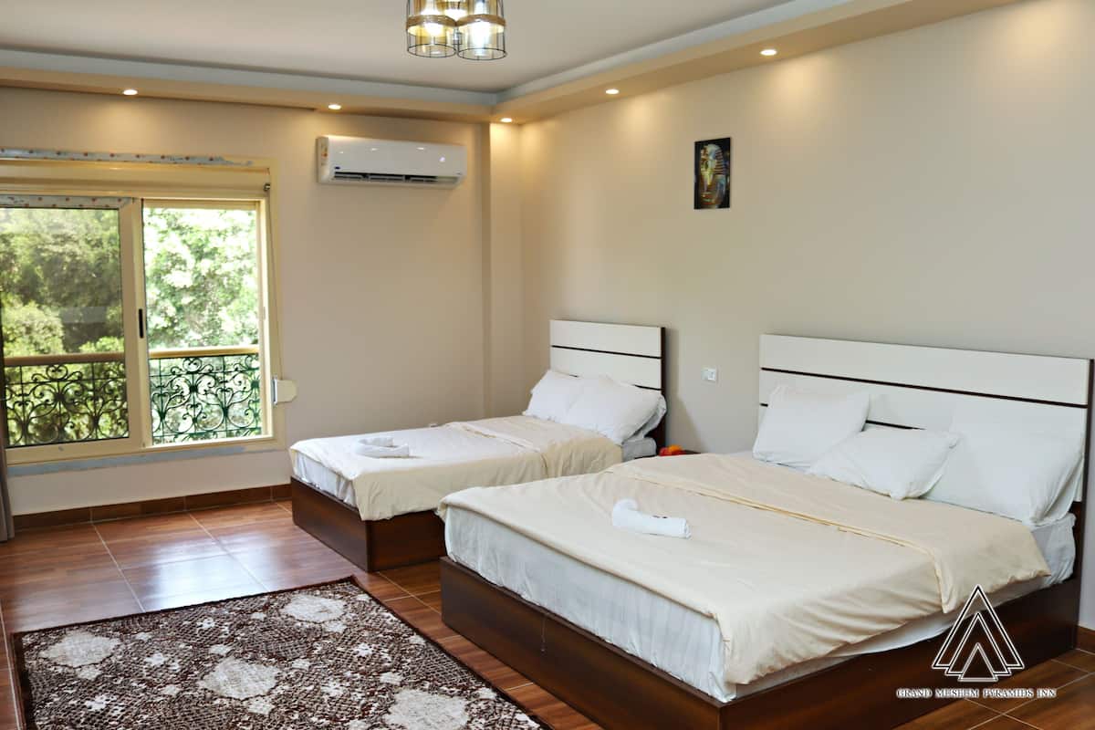 Habitación de hotel con dos camas, un ventanal con vistas a la vegetación, un ventilador de techo y un equipo de aire acondicionado.