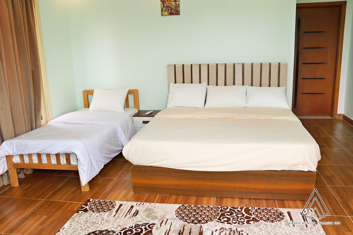 Habitación de hotel con una cama grande, una cama más pequeña, una mesita de noche y piso de madera.