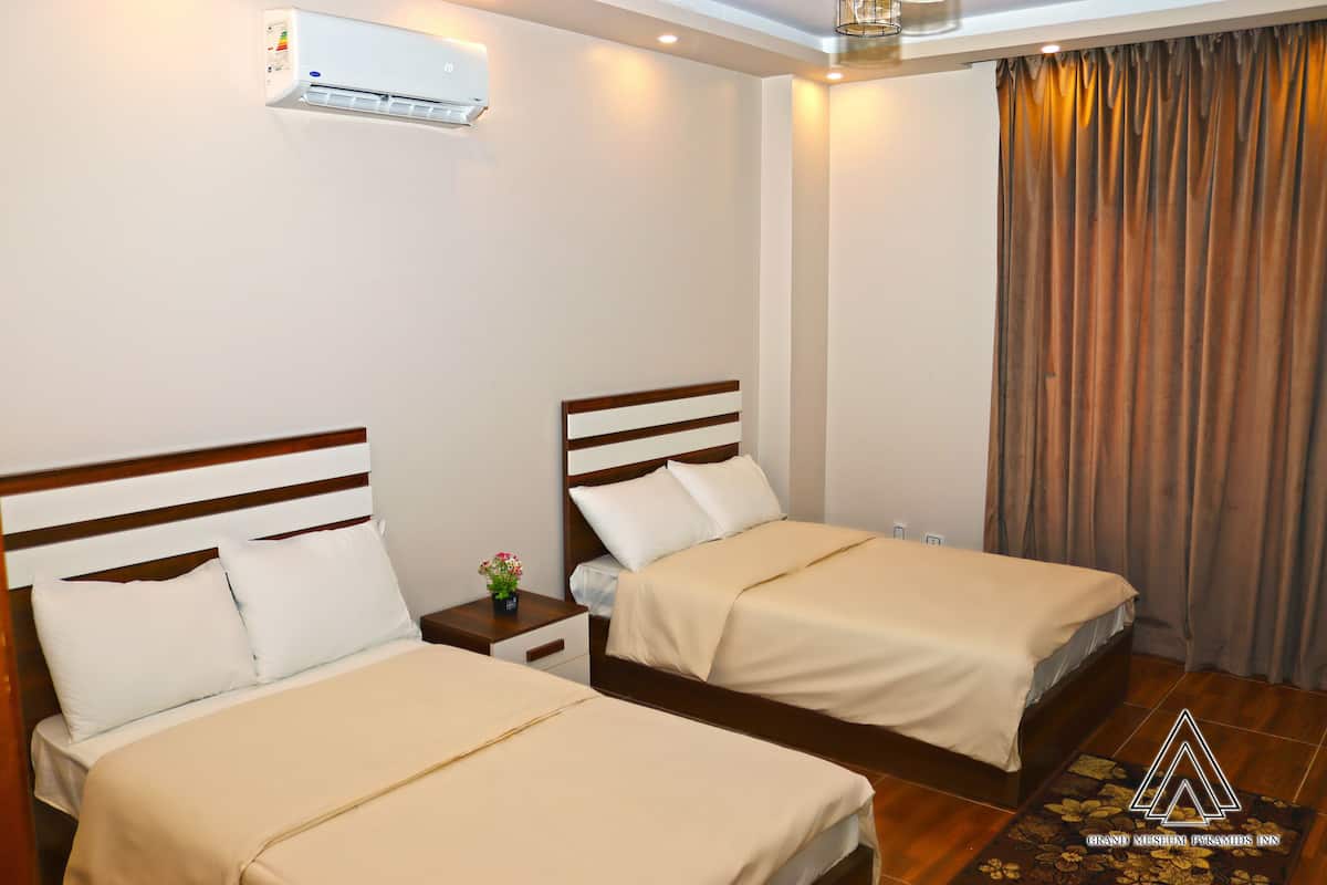 Habitación de hotel con dos camas, una mesita de noche con lámpara, aire acondicionado y cortina.