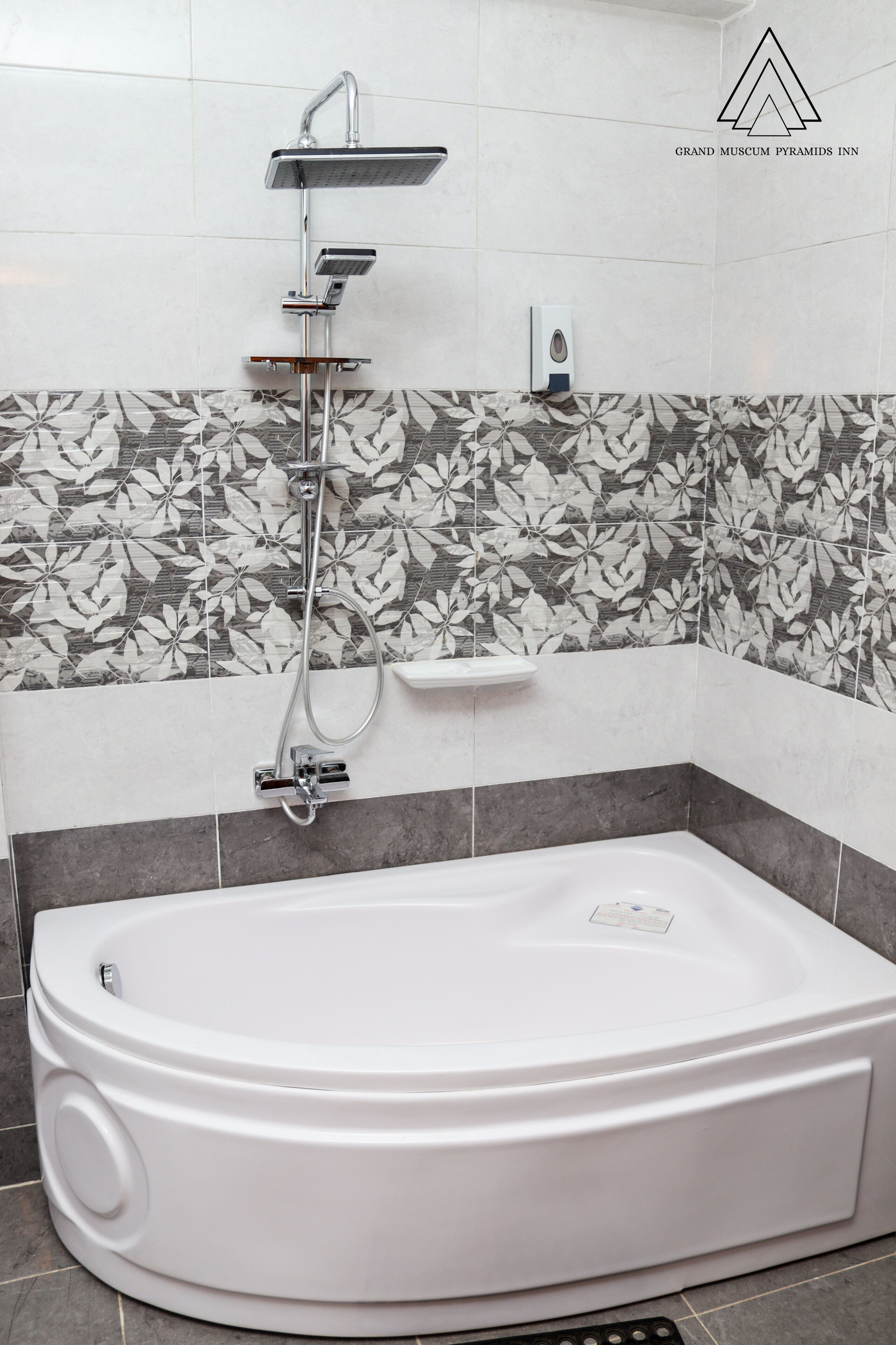 Un baño moderno con una bañera independiente, un cabezal de ducha de mano y un grifo empotrado en la pared. Las paredes están cubiertas de azulejos con un estampado floral y hay un estante pequeño sobre la bañera.