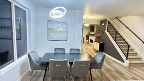 Un comedor moderno con una mesa oscura y sillas grises, un ventanal grande y una escalera que sube a un nivel superior.
