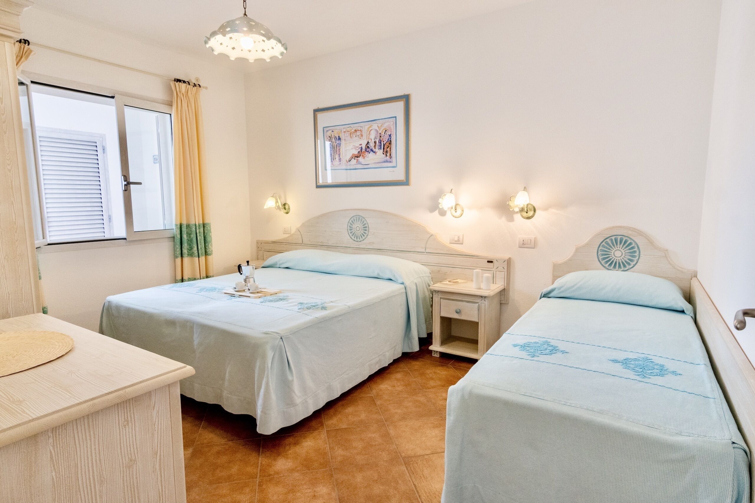 A bedroom with two beds, a bedside table, a nightstand, a lamp, and a window with curtains.