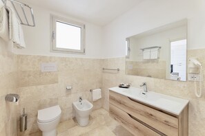 Une salle de bain moderne comprenant des toilettes, un bidet, un meuble-lavabo avec un miroir et une fenêtre.