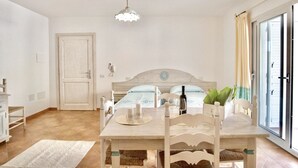 A room with a bed, a dining table with chairs, a chandelier, and a view through a glass door. - Apartments with air conditioning in Orosei (Orosei)