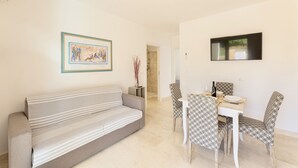 A living room with a sofa, dining table, chairs, a TV, and a framed picture on the wall. - Apartments with air conditioning in Orosei (Orosei)