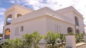 A white building with arched windows and balconies, surrounded by greenery. - Apartments with air conditioning in Orosei (Orosei)