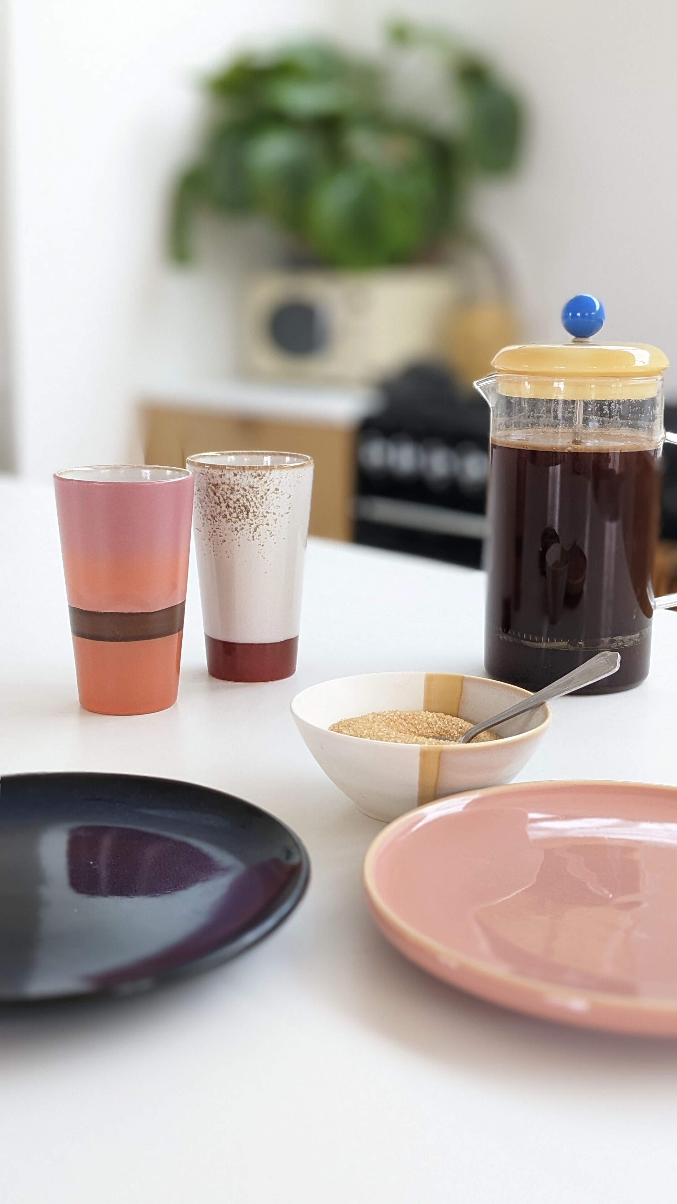A table with two coffee cups, a coffee pot, a bowl of sugar, and a spoon.