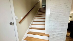 A staircase with wooden steps and white walls, leading to a room with a white brick accent wall. - Coveside: Town Cove Waterfront (Orleans)