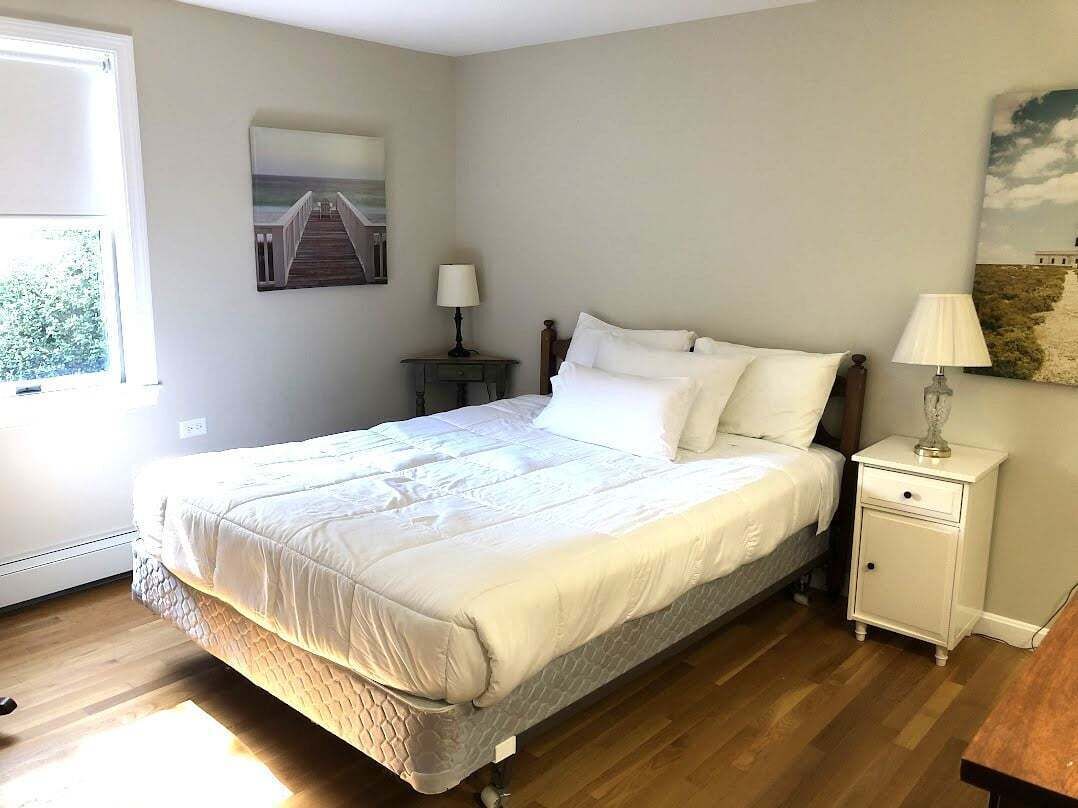 Un dormitorio con cama, mesita de noche, lámpara y un cuadro en la pared.