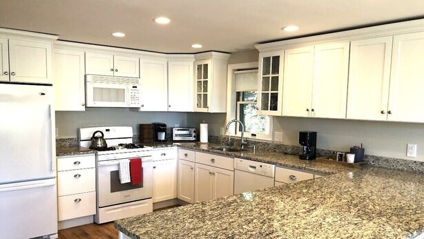 A modern kitchen with white cabinets, granite countertops, a built-in microwave, a stove, and a sink. - Coveside: Town Cove Waterfront (Orleans)