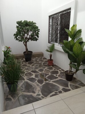 A small courtyard with potted plants, a stone floor, and a window with decorative iron bars. - Beautiful New Casita-Ajijic West 360 Degree View of Lake/Mountains (Ajijic)
