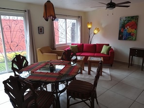 A living room with a red sofa, a glass-top dining table, and a ceiling fan. - Beautiful New Casita-Ajijic West 360 Degree View of Lake/Mountains (Ajijic)